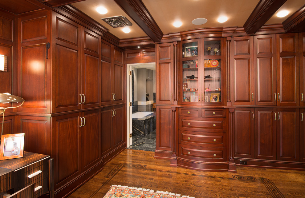 Foto de vestidor unisex clásico extra grande con armarios con paneles con relieve, puertas de armario de madera en tonos medios y suelo de madera oscura