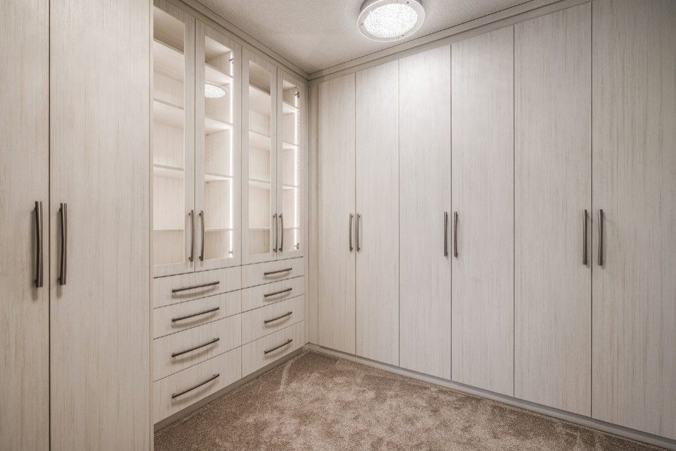 Ejemplo de armario vestidor unisex clásico de tamaño medio con armarios con paneles lisos, puertas de armario de madera clara, moqueta y suelo beige