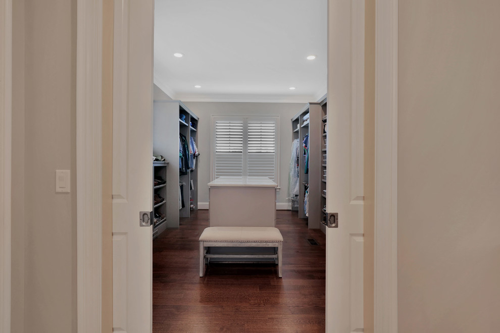 Ejemplo de armario vestidor unisex de estilo americano grande con armarios con paneles empotrados, puertas de armario grises y suelo de madera en tonos medios