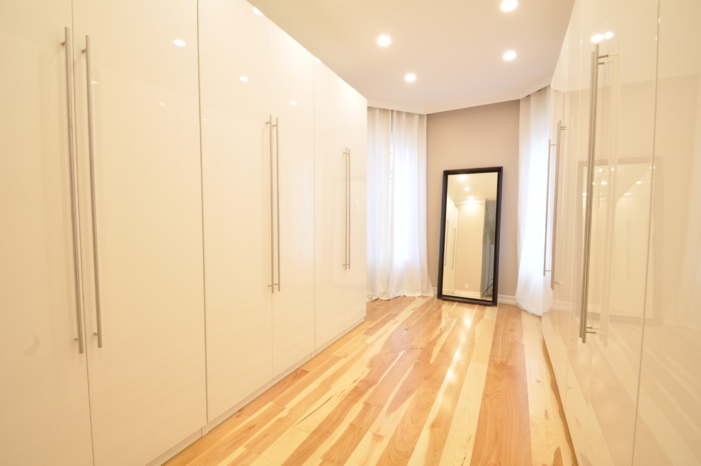 Foto de armario vestidor unisex minimalista grande con armarios con paneles lisos, puertas de armario blancas y suelo de madera clara