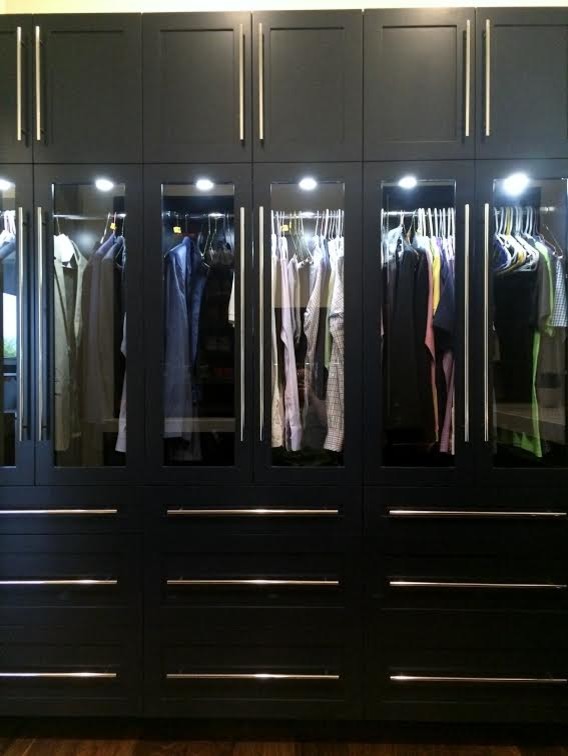Immagine di una cabina armadio unisex minimal di medie dimensioni con ante di vetro, ante nere e parquet scuro