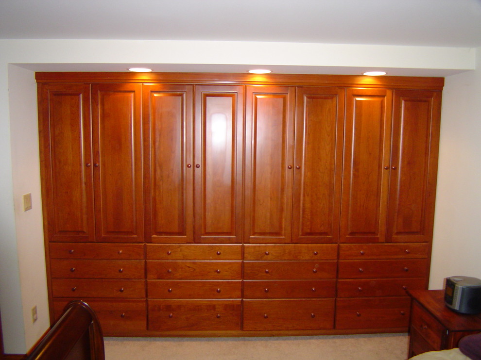 Ejemplo de armario unisex tradicional de tamaño medio con armarios con paneles empotrados, puertas de armario de madera oscura y moqueta