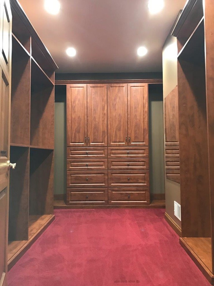 Foto de armario vestidor unisex clásico grande con armarios con paneles con relieve, puertas de armario de madera en tonos medios, suelo rojo y moqueta