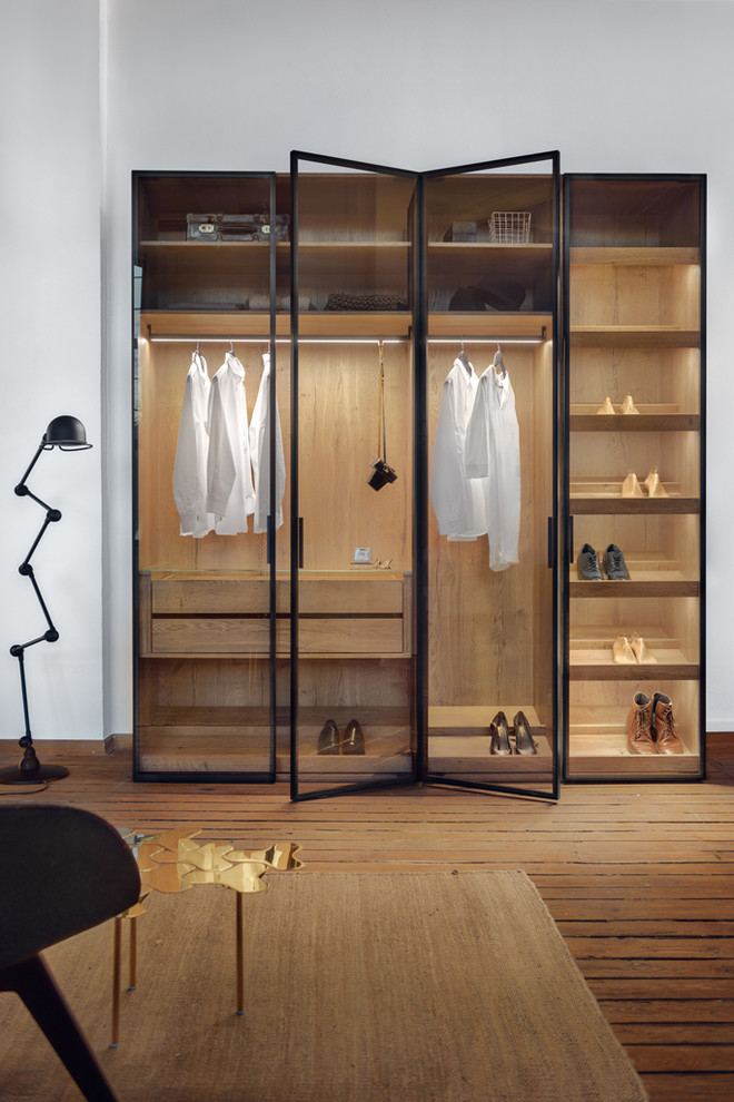 This is an example of a large modern gender neutral walk-in wardrobe in Boston with glass-front cabinets, medium wood cabinets, light hardwood flooring and brown floors.
