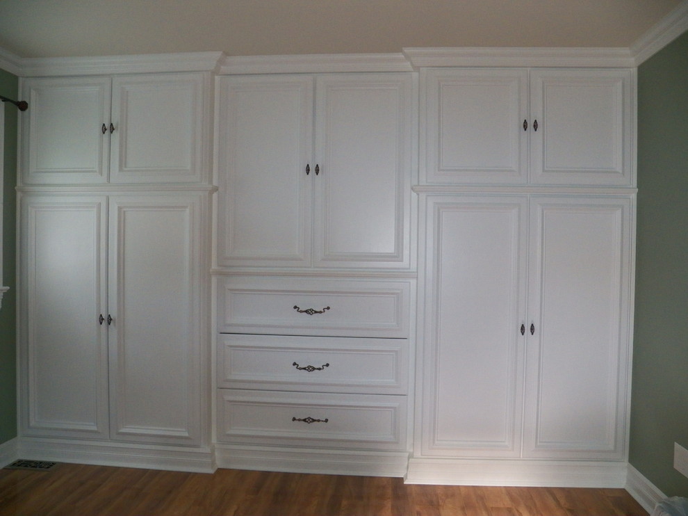 Modelo de armario vestidor unisex actual grande con armarios con paneles empotrados, puertas de armario blancas y suelo de madera en tonos medios