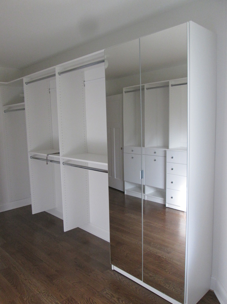 This is an example of a large classic gender neutral dressing room in New York with glass-front cabinets, white cabinets and carpet.