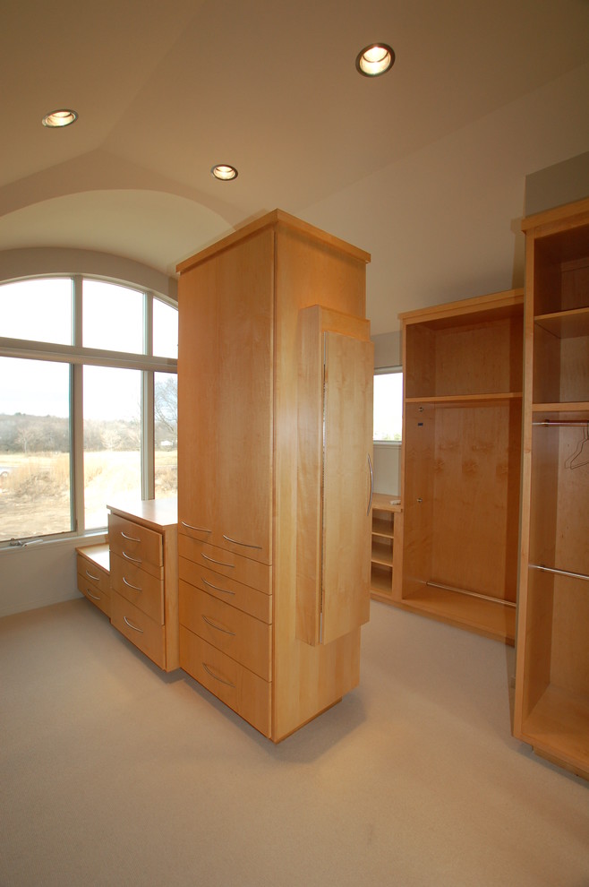 This is an example of an expansive contemporary walk-in wardrobe in Milwaukee with flat-panel cabinets, light wood cabinets and carpet.