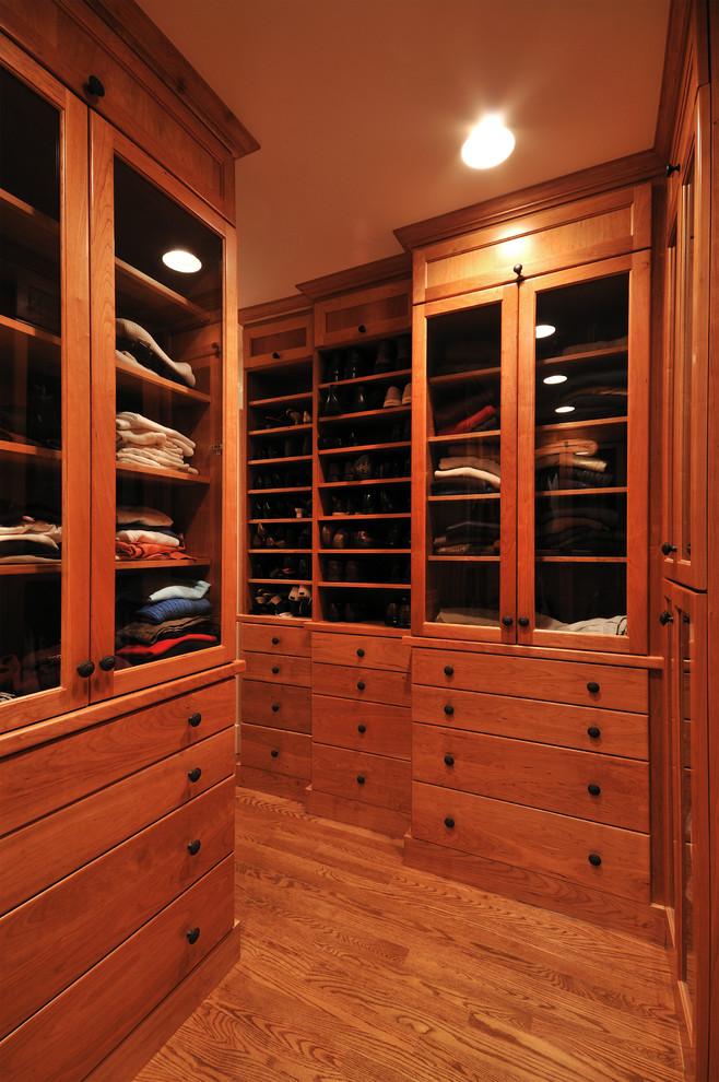 Diseño de armario vestidor unisex clásico de tamaño medio con armarios con paneles lisos, puertas de armario de madera oscura y suelo de madera en tonos medios