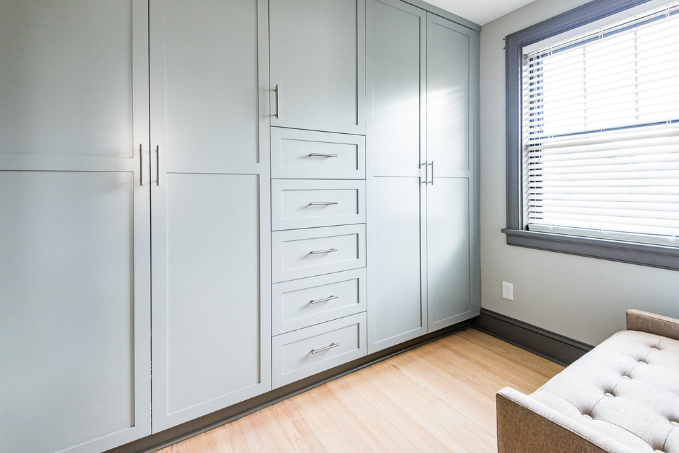 Diseño de armario moderno de tamaño medio con armarios estilo shaker, puertas de armario azules, suelo de madera clara y suelo marrón