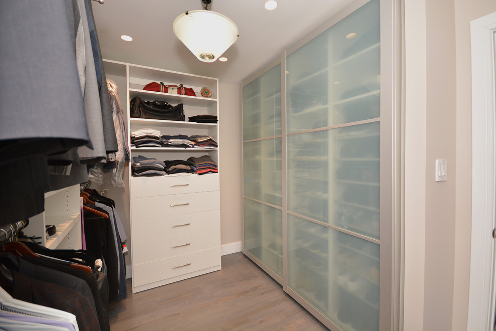 Diseño de armario vestidor de hombre actual pequeño con armarios tipo vitrina, puertas de armario blancas, suelo de madera en tonos medios y suelo gris