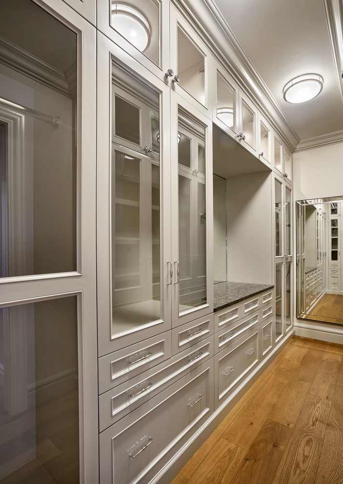Diseño de armario vestidor unisex clásico grande con armarios con paneles empotrados, puertas de armario grises y suelo de madera clara