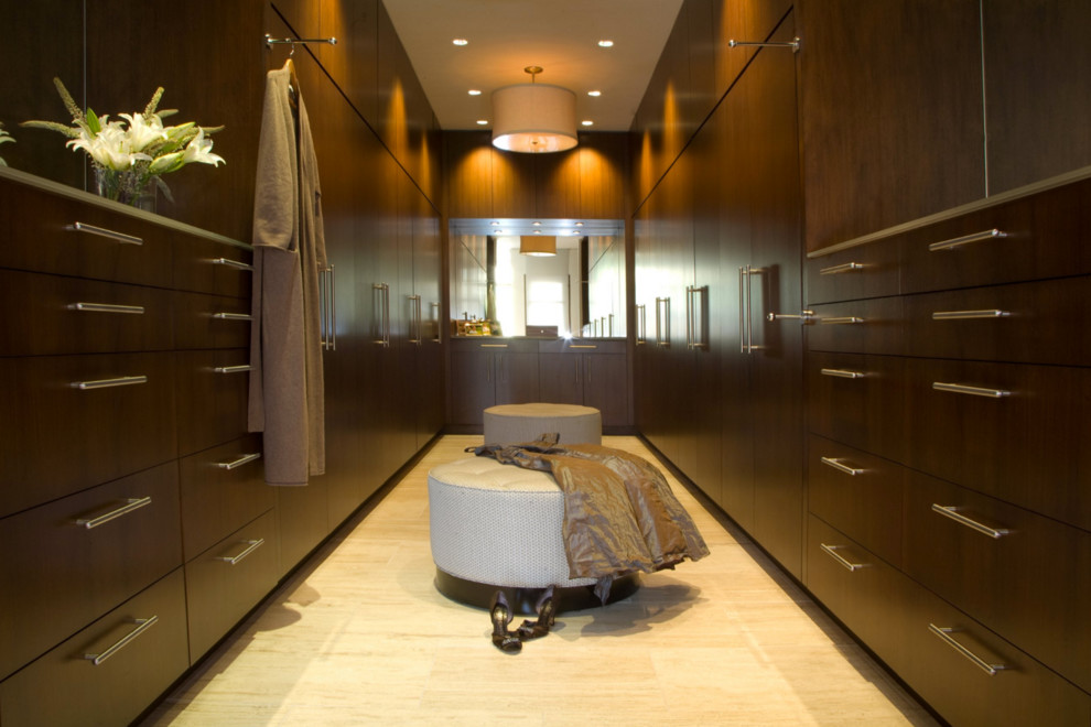 This is an example of a large contemporary gender neutral dressing room in Other with flat-panel cabinets, dark wood cabinets and travertine flooring.