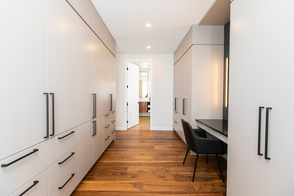 Ispirazione per un'ampia cabina armadio unisex design con ante lisce, ante grigie, pavimento in legno massello medio e pavimento marrone