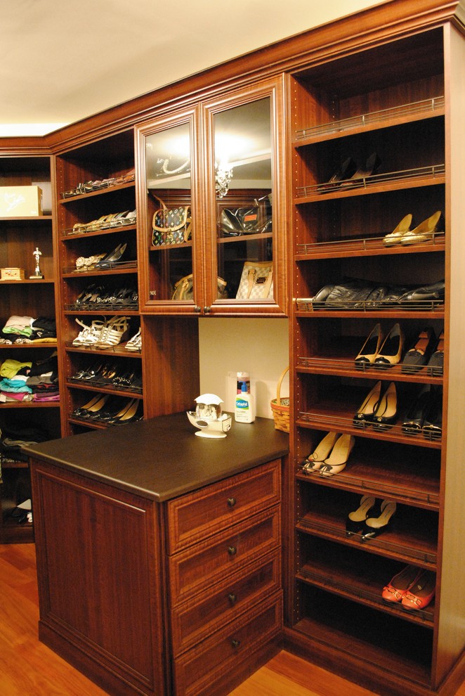 This is an example of a large classic walk-in wardrobe for women in DC Metro with medium wood cabinets, medium hardwood flooring and glass-front cabinets.
