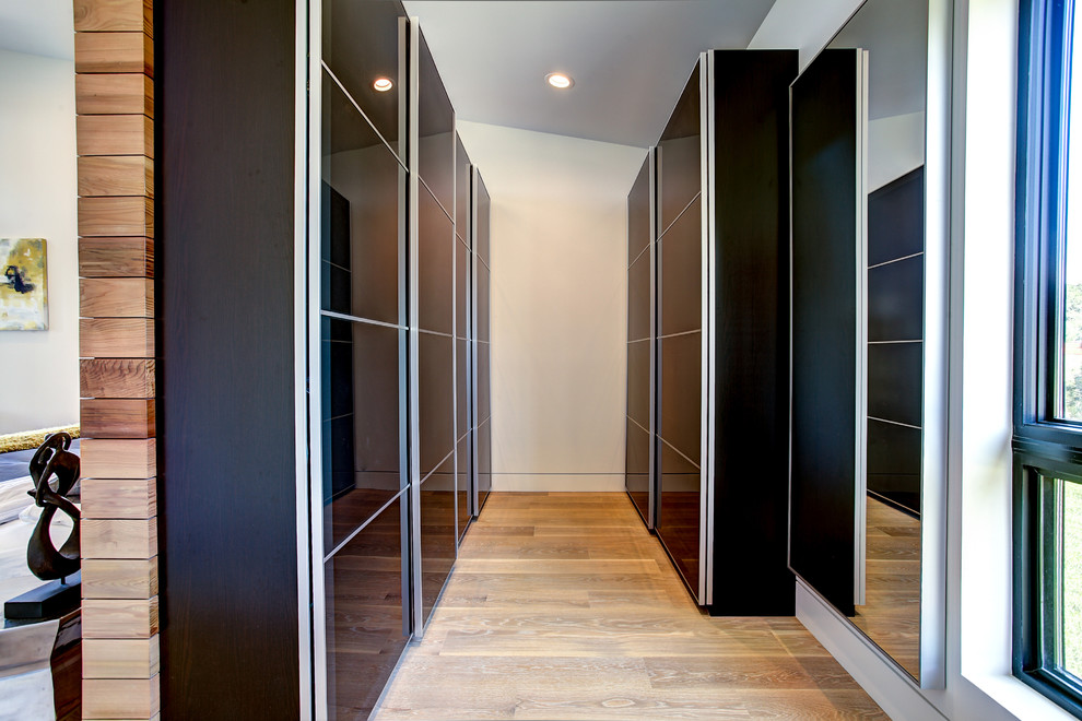 Diseño de armario vestidor unisex contemporáneo de tamaño medio con armarios con paneles lisos, puertas de armario negras, suelo de madera clara y suelo beige