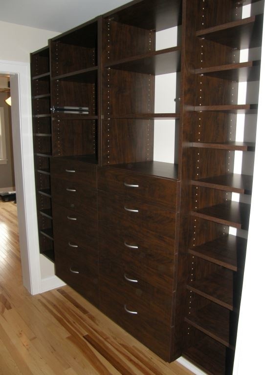 Modelo de armario vestidor clásico grande con armarios con paneles lisos, puertas de armario de madera en tonos medios, suelo de madera clara y suelo marrón