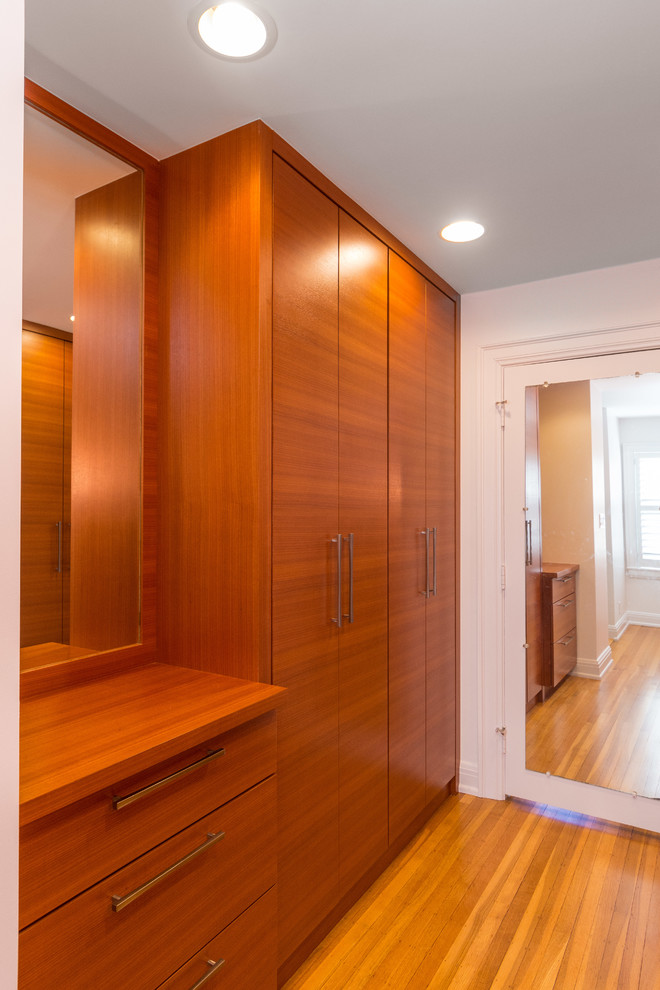Ejemplo de vestidor unisex actual de tamaño medio con armarios con paneles lisos, puertas de armario de madera oscura, suelo de madera clara y suelo marrón