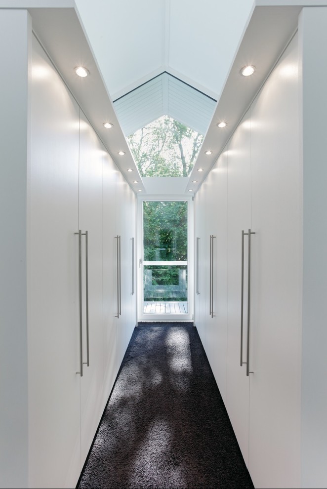 На фото: большая гардеробная комната унисекс в современном стиле с плоскими фасадами, белыми фасадами, ковровым покрытием и черным полом