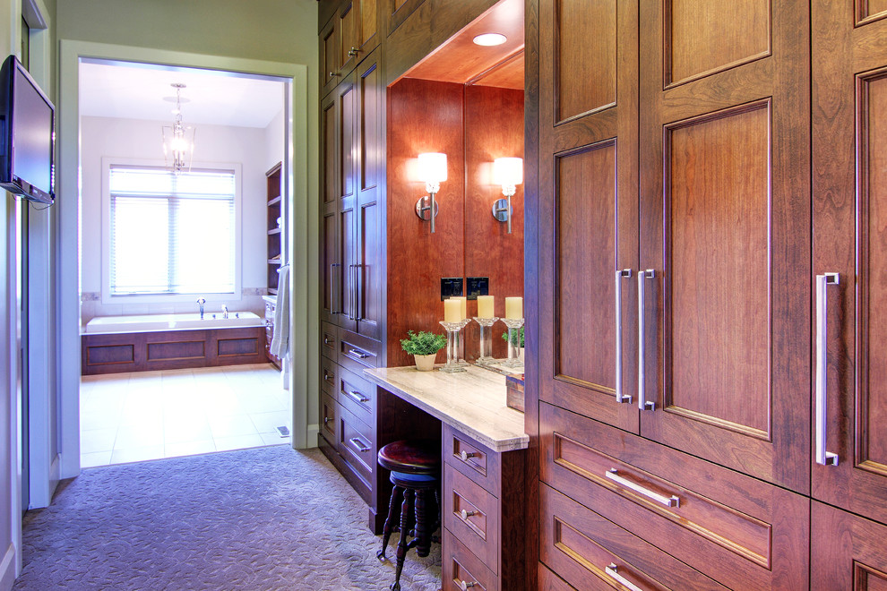 Aménagement d'un grand dressing room classique en bois brun neutre avec moquette et un placard avec porte à panneau encastré.