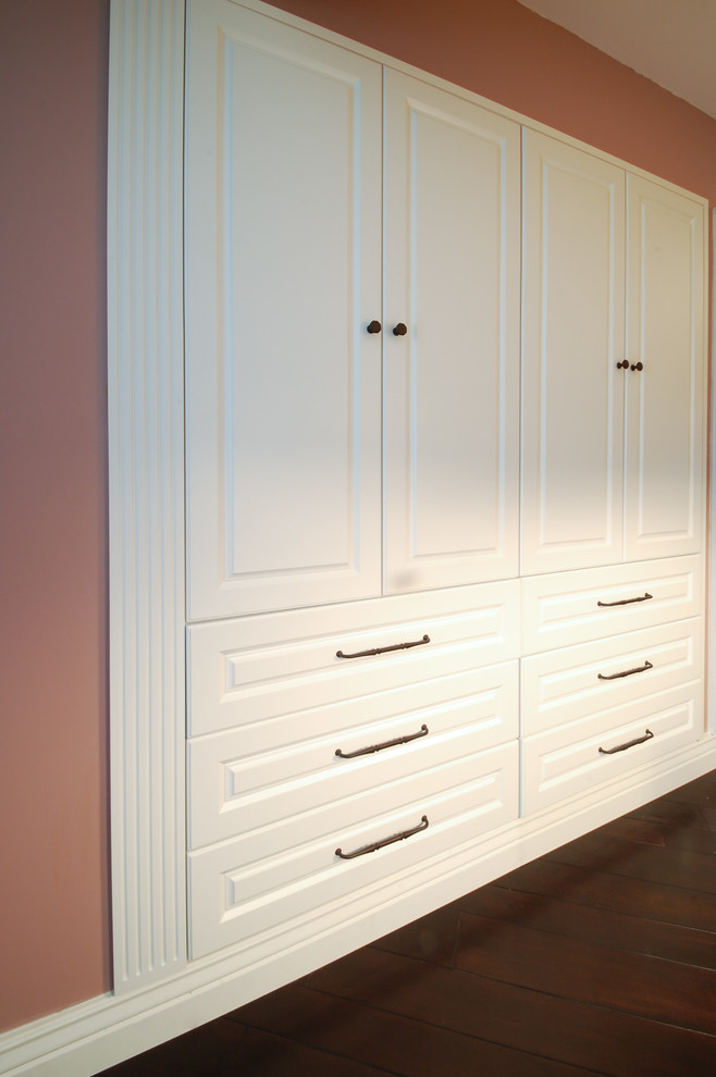 Imagen de armario de mujer tradicional de tamaño medio con armarios con paneles con relieve, puertas de armario blancas y suelo de madera oscura