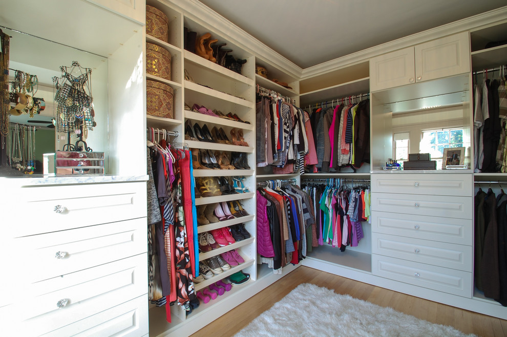 Diseño de armario vestidor unisex tradicional grande con armarios con paneles con relieve, puertas de armario blancas y suelo de madera clara