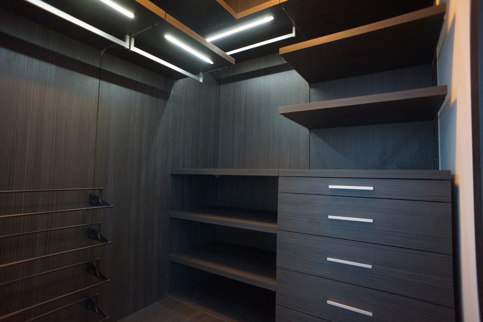 На фото: гардеробная комната среднего размера, унисекс в стиле модернизм с плоскими фасадами, темными деревянными фасадами и темным паркетным полом с