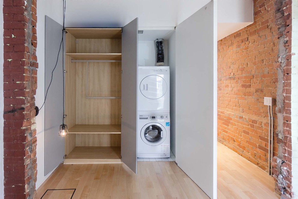 Diseño de armario unisex minimalista pequeño con armarios con paneles lisos, puertas de armario blancas y suelo de madera clara