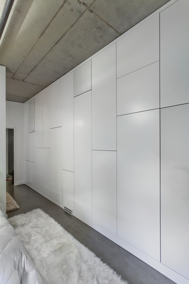 Ejemplo de armario unisex grande con suelo de cemento, armarios con paneles lisos y puertas de armario blancas