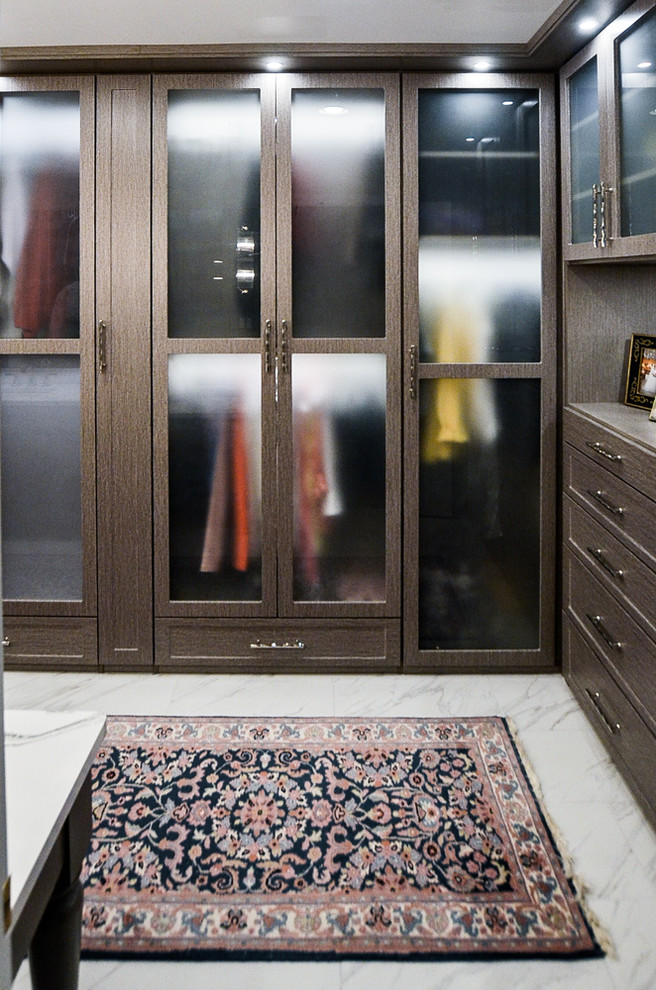 Cette image montre un grand dressing room en bois foncé neutre avec un placard à porte vitrée, un sol en marbre et un sol blanc.