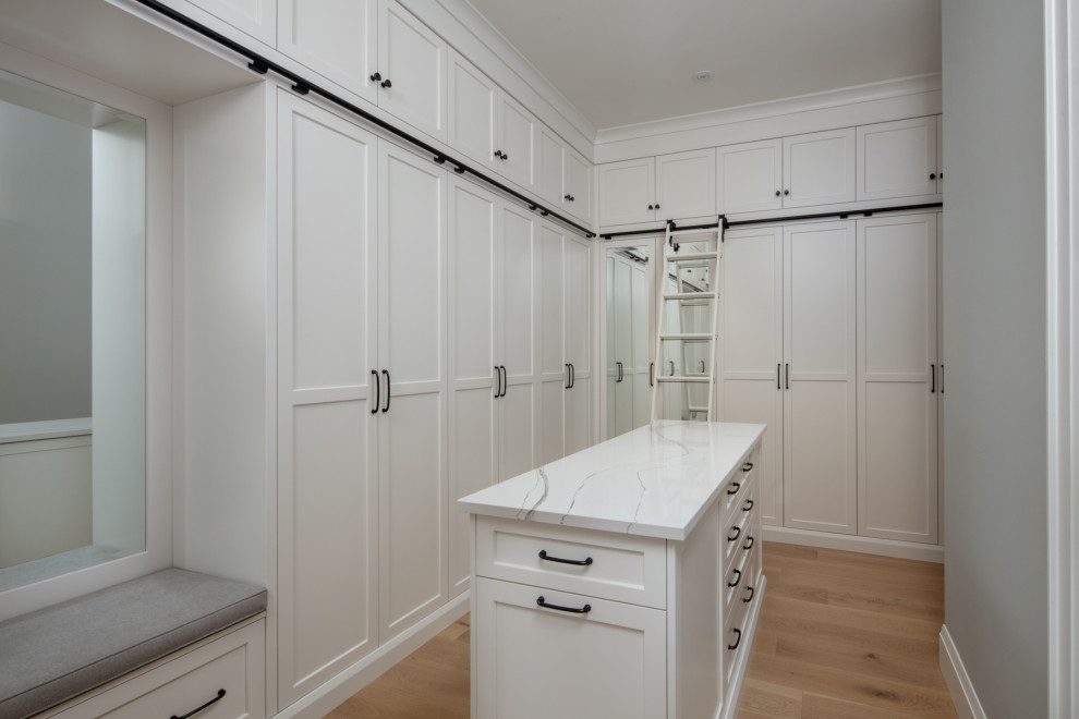 Inspiration for an expansive classic gender neutral walk-in wardrobe in Toronto with shaker cabinets, white cabinets, light hardwood flooring and beige floors.
