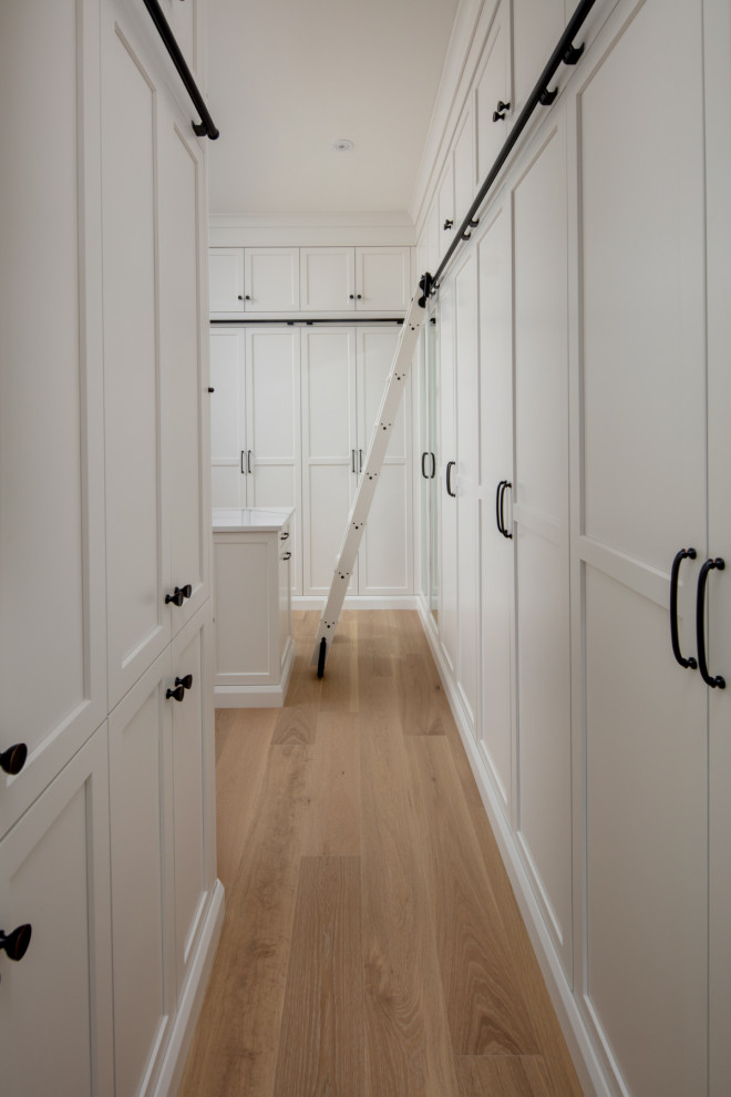Expansive classic gender neutral walk-in wardrobe in Toronto with shaker cabinets, white cabinets, light hardwood flooring and beige floors.