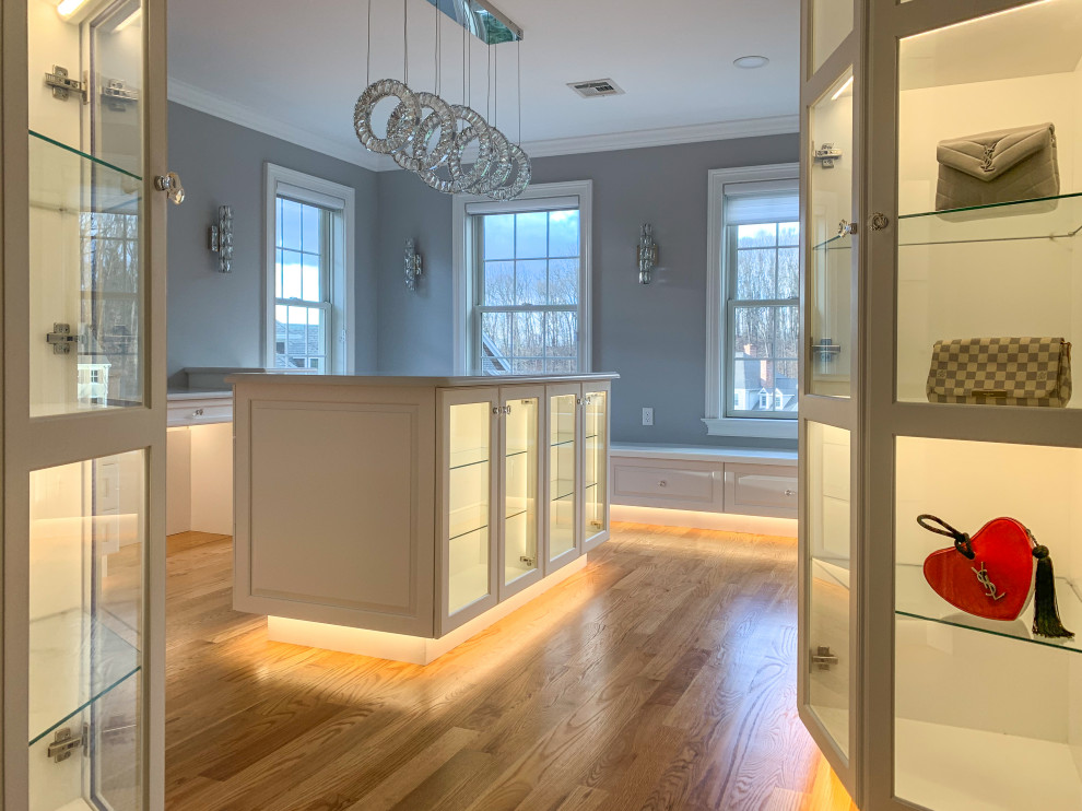 Inspiration for a large traditional dressing room for women in Bridgeport with glass-front cabinets, white cabinets, medium hardwood flooring and brown floors.