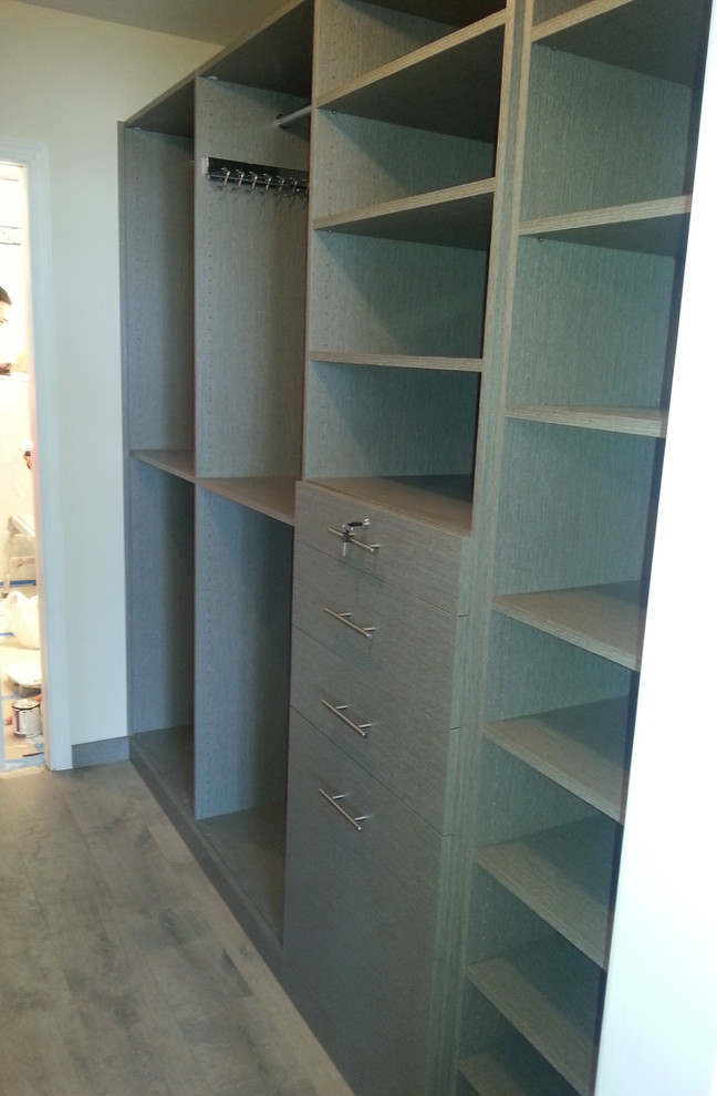 Modelo de armario vestidor unisex contemporáneo de tamaño medio con armarios con paneles lisos, puertas de armario grises, suelo de madera clara y suelo beige