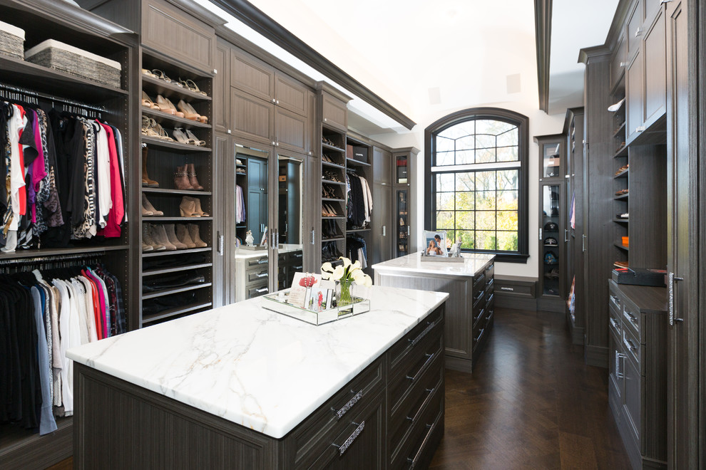 Example of a large transitional gender-neutral dark wood floor and brown floor walk-in closet design in New York with recessed-panel cabinets and gray cabinets