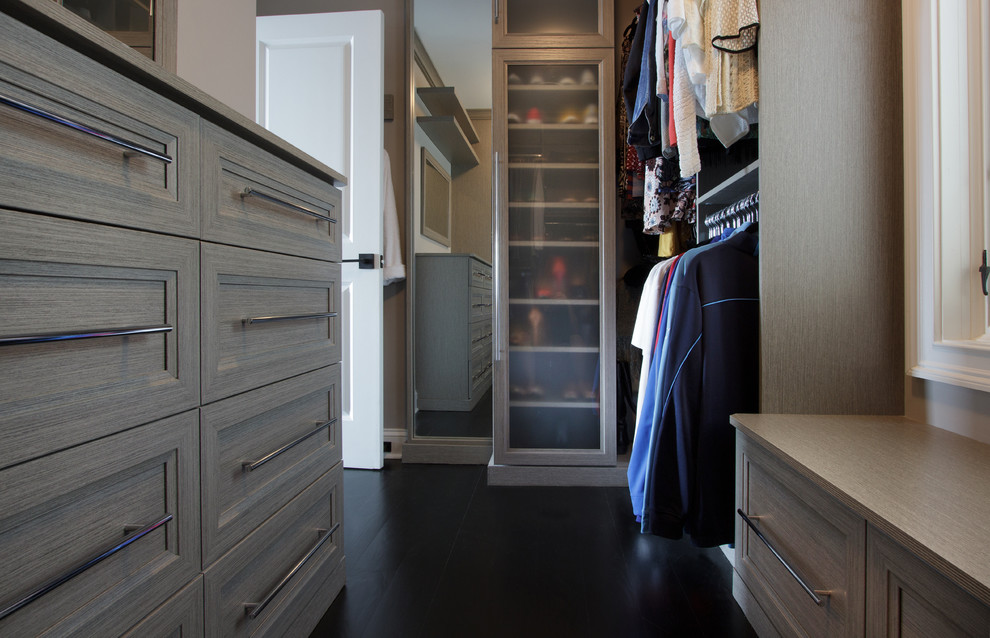 Diseño de armario vestidor unisex tradicional renovado pequeño con armarios con paneles empotrados, puertas de armario grises y suelo de madera oscura