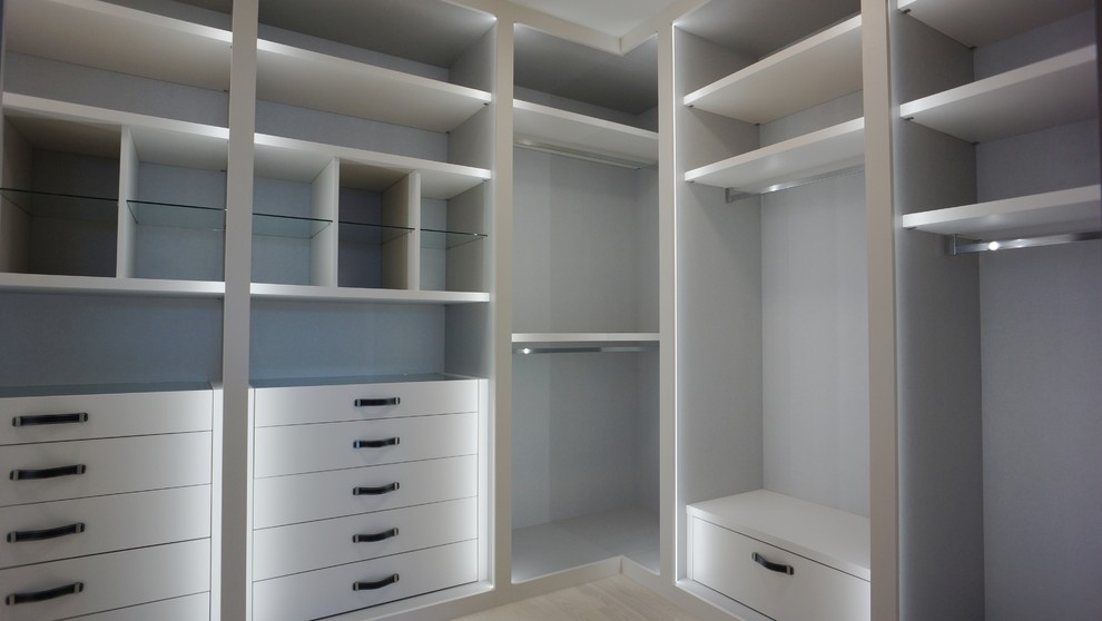 Diseño de armario vestidor unisex moderno de tamaño medio con armarios con paneles lisos, puertas de armario blancas y suelo de madera clara