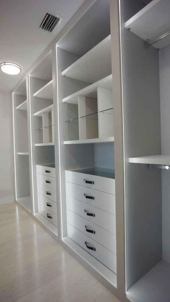 This is an example of a medium sized modern gender neutral walk-in wardrobe in Miami with flat-panel cabinets, white cabinets and light hardwood flooring.