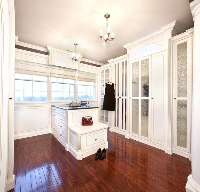 Modelo de armario vestidor tradicional grande con armarios tipo vitrina, puertas de armario blancas y suelo de madera en tonos medios