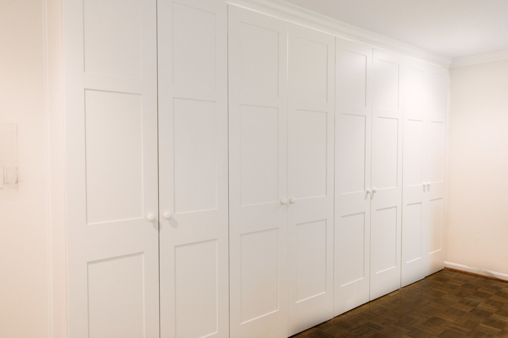 Idées déco pour un placard dressing classique de taille moyenne et neutre avec un placard à porte plane, des portes de placard blanches et un sol en bois brun.