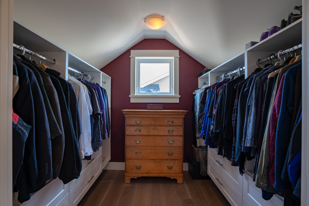 Diseño de armario vestidor unisex tradicional de tamaño medio con armarios estilo shaker, puertas de armario blancas, suelo de madera en tonos medios y suelo marrón