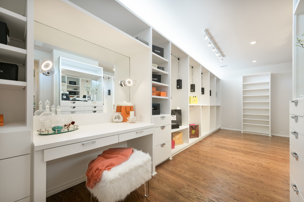 Contemporary walk-in wardrobe for women in Houston with flat-panel cabinets, white cabinets, medium hardwood flooring and brown floors.