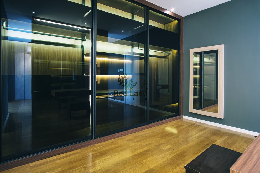Modelo de vestidor unisex moderno con armarios tipo vitrina, puertas de armario de madera en tonos medios, suelo de madera en tonos medios y suelo marrón