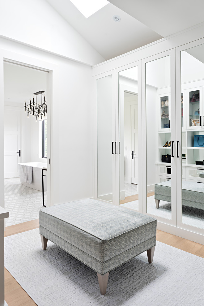 Inspiration pour un dressing room traditionnel pour une femme avec un placard avec porte à panneau encastré, des portes de placard blanches, parquet clair et un plafond voûté.