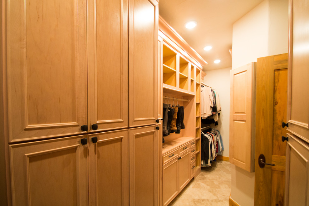 Diseño de armario vestidor unisex tradicional grande con armarios con paneles con relieve, puertas de armario de madera clara, suelo de travertino y suelo beige