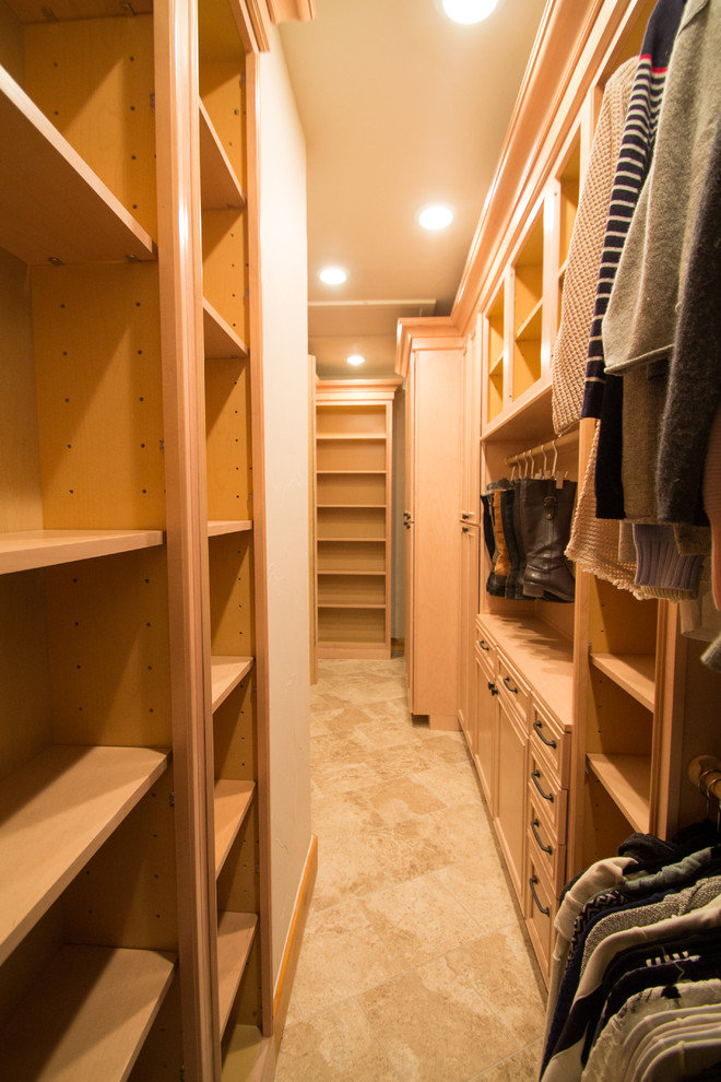 This is an example of a large classic gender neutral walk-in wardrobe in Denver with raised-panel cabinets, light wood cabinets, travertine flooring and beige floors.