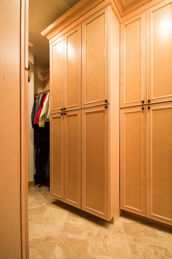 Imagen de armario vestidor unisex clásico grande con armarios con paneles con relieve, puertas de armario de madera clara, suelo de travertino y suelo beige