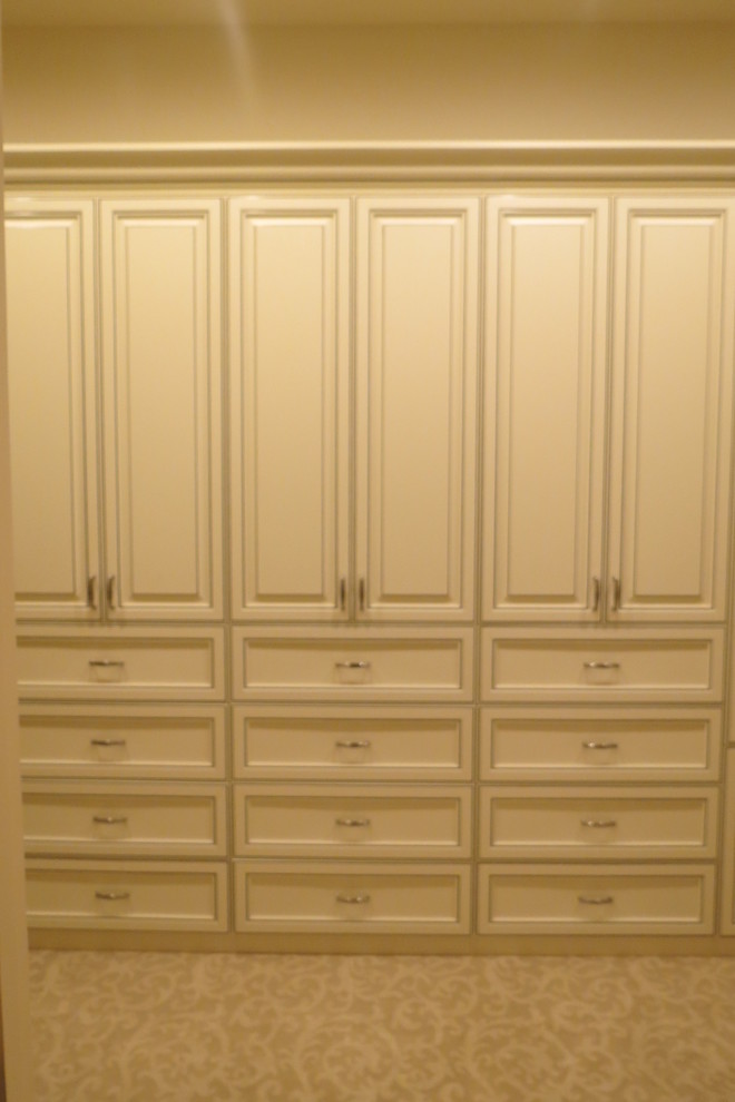 Imagen de armario vestidor de mujer clásico grande con armarios con paneles con relieve, moqueta y puertas de armario beige