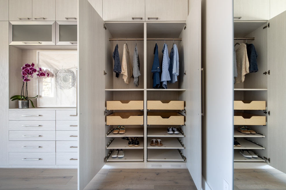 Diseño de armario unisex actual pequeño con armarios con paneles lisos, puertas de armario de madera clara, suelo de madera clara y suelo marrón