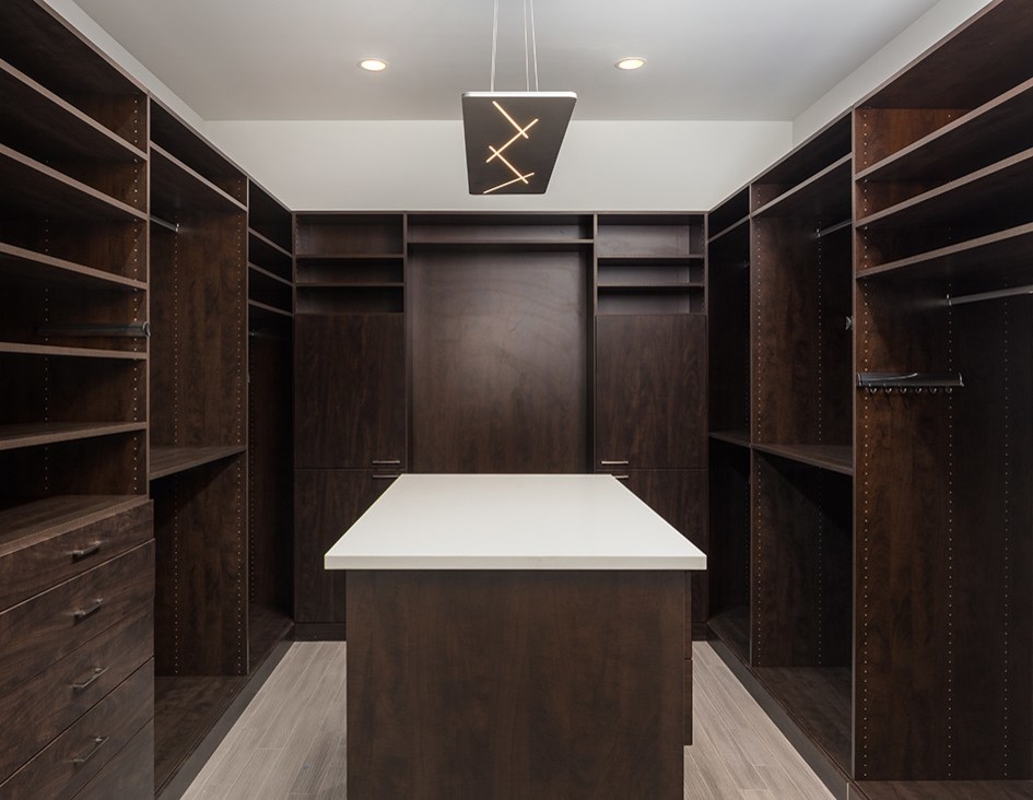 Large trendy gender-neutral porcelain tile and brown floor walk-in closet photo in DC Metro with flat-panel cabinets and dark wood cabinets