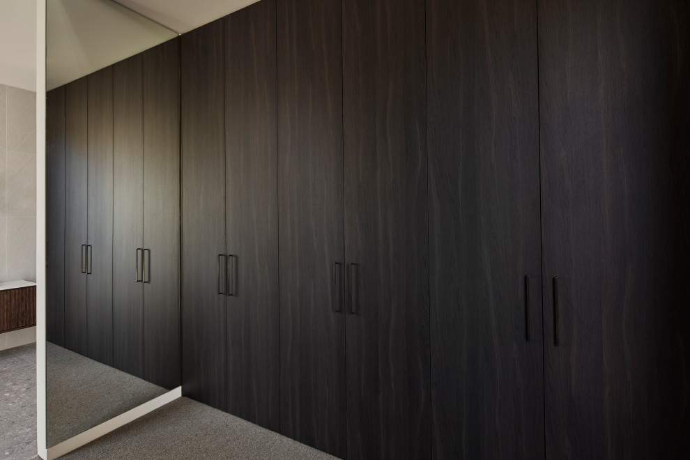 Cette image montre un grand dressing design neutre avec un placard à porte plane, des portes de placard marrons, moquette et un sol gris.